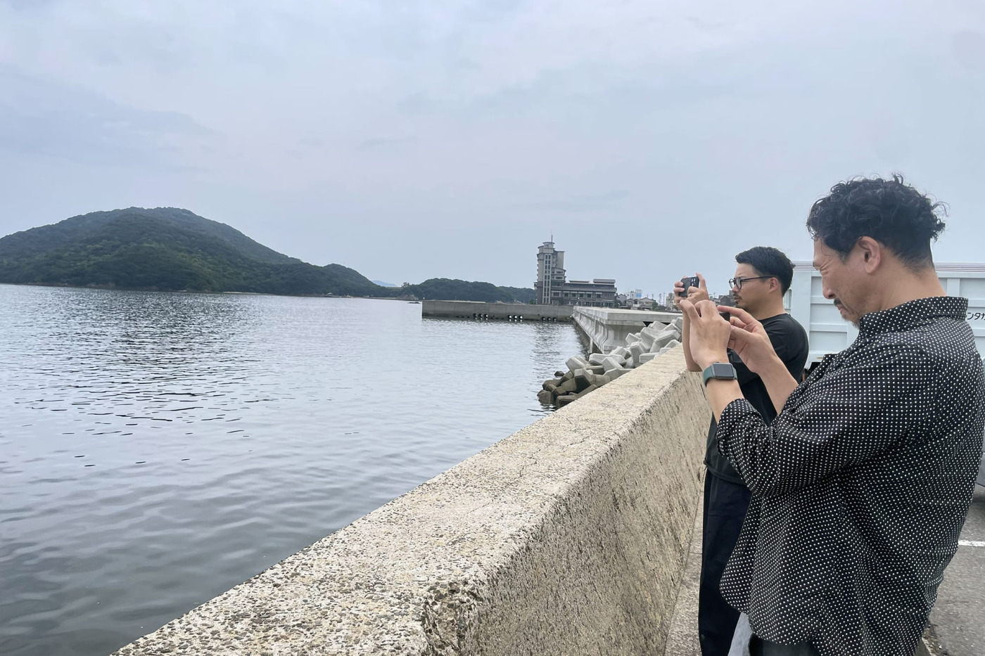 工場にいく途中。映画「崖の上のポニョ」の舞台とも言われる、広島県福山市にある港町、鞆の浦で休憩中の、カメラマン兼下さん（奥）と、ディレクターの石田。