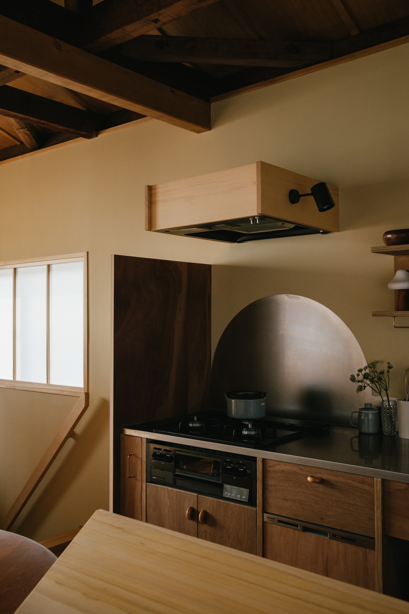 この​木の​素材感が​特徴的な​レンジフード、​実は​『フラットレンジフード』​ブラックを​無垢の​板で​囲った​もの。​コンパクトな​フォルムは​そのままに、​ブラックの​強さを​和らげ、馴染ませてくれています。​