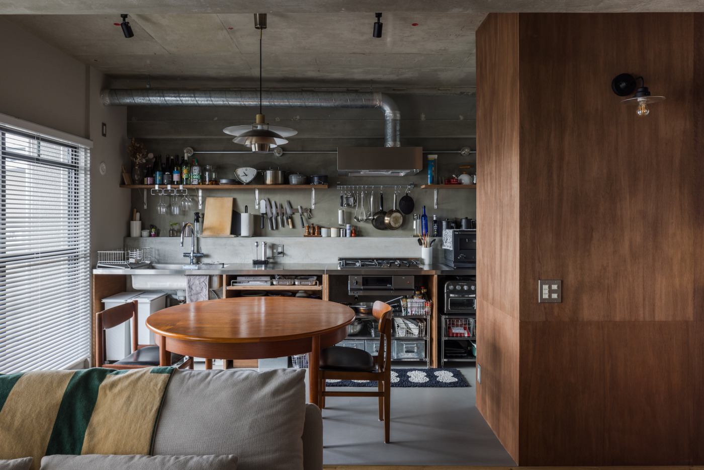 ラワンの壁に映える『アルミニウムブラケットライト』。素朴な佇いが空間に馴染み、リビングの入り口をやさしく照らします。