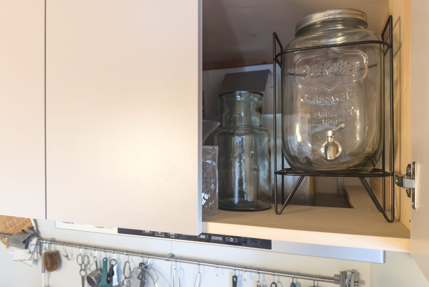 吊り戸棚を開けると、レンジフードのダクトカバーが見える。手前は瓶置きとして利用。