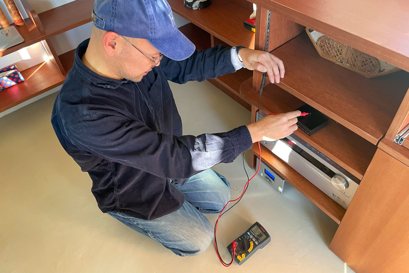 3のステップで、黒い方の先（プラグ）を指で軽く握り、赤い方を黒い機器の金属部にあてて電圧を測ります。（※注）